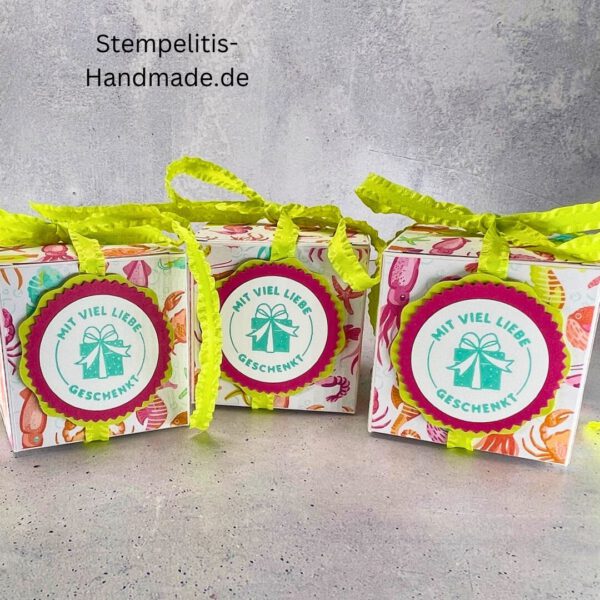 Handdekorierte Geschenkschachtel mit Schleife von oben, Geschenkschachtel mit liebevollem Aufkleber “Mit viel Liebe verschenkt”, Detailansicht Schleife auf Geschenkschachtel, Seitenansicht Geschenkschachtel mit buntem Designpapier, Offene Geschenkbox zum Befüllen, Geschenkschachtel auf hellem Hintergrund mit Dekorband, Handgemachte Geschenkverpackung mit grünem Band und Etikett